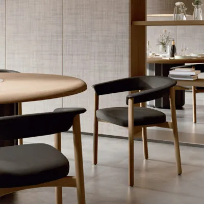 Lash wooden chair design in natural oak with black upholstered seat, detail view alongside a round oak table in a contemporary restaurant lounge — Sabree Italian design