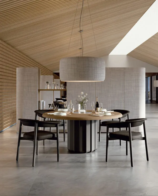 Table ronde de design Sabree avec plateau plaqué chêne et pied central sculpté noir, dressée dans un restaurant resort avec plafond en bois