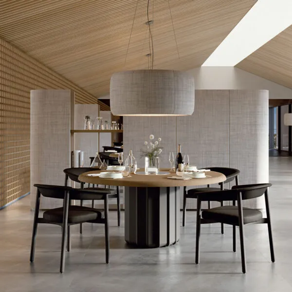 Table ronde de design Sabree avec plateau plaqué chêne et pied central sculpté noir, dressée dans un restaurant resort avec plafond en bois