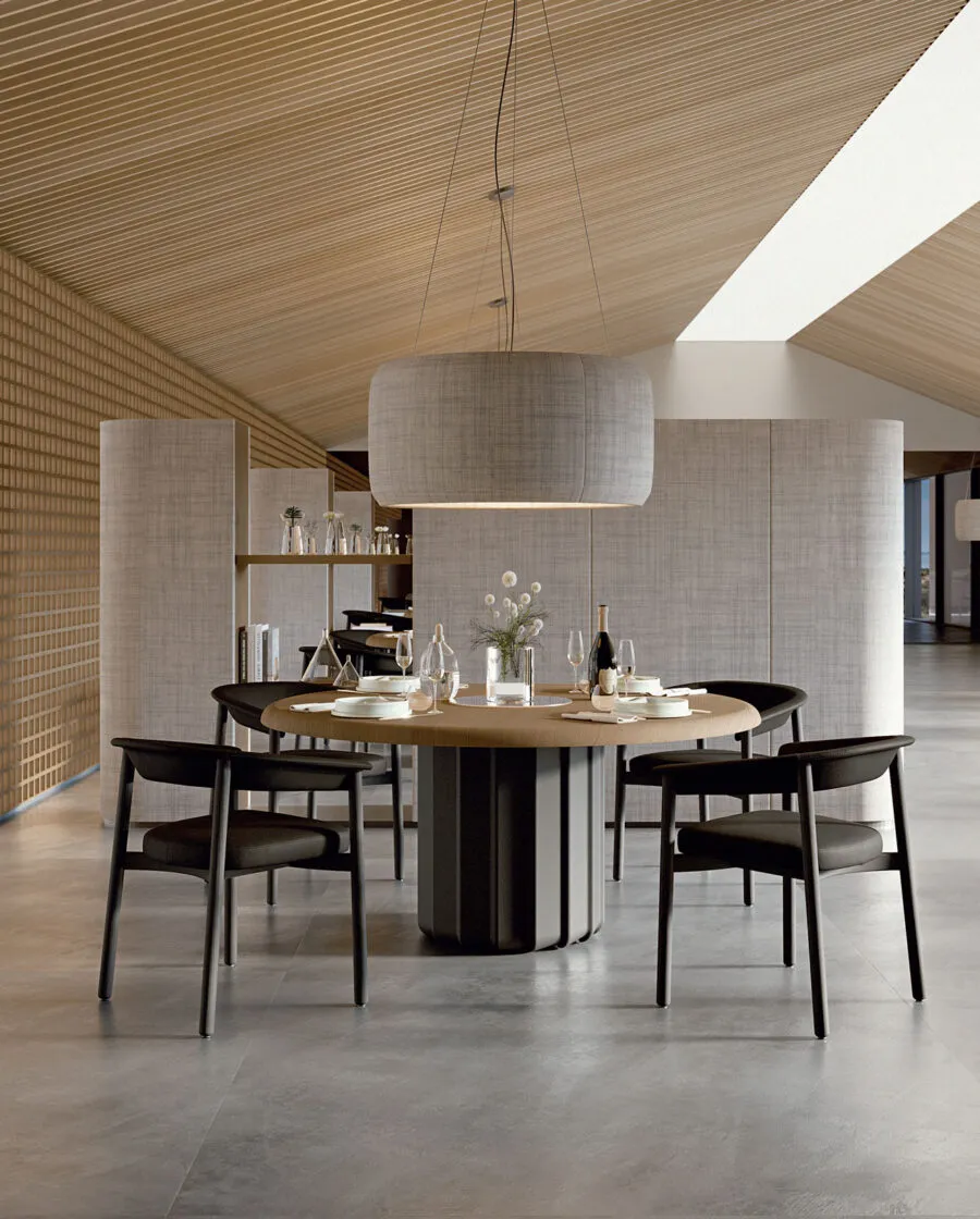 Table ronde design Sabree à pied central avec plateau en chêne et base noire entourée de chaises Lash dans un restaurant resort avec plafond en bois — Frezza contract