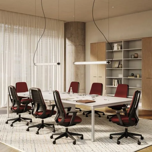 Sedie ufficio ergonomiche Areca Fabric rivestite in tessuto rosso attorno a un tavolo riunioni bianco, in un ufficio con tende e libreria in legno