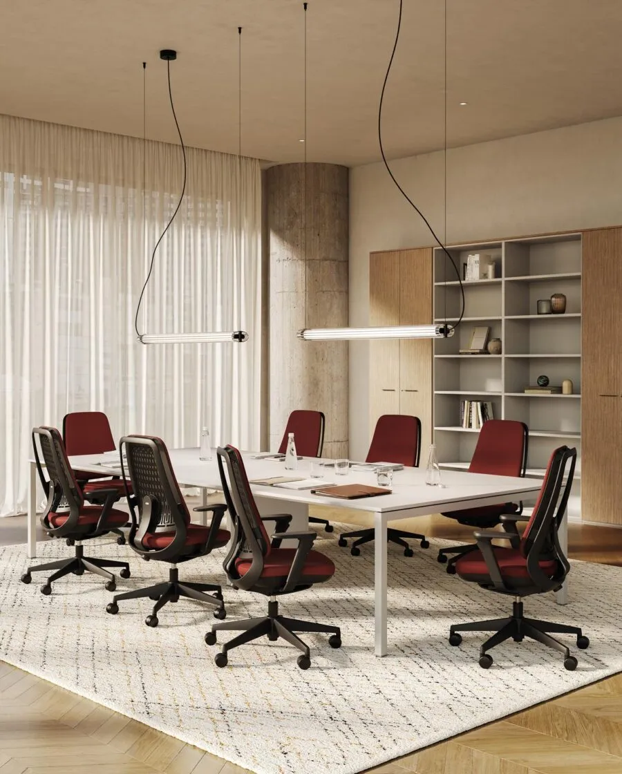Sedie ufficio ergonomiche Areca Fabric rivestite in tessuto rosso attorno a un tavolo riunioni bianco, in un ufficio con tende e libreria in legno