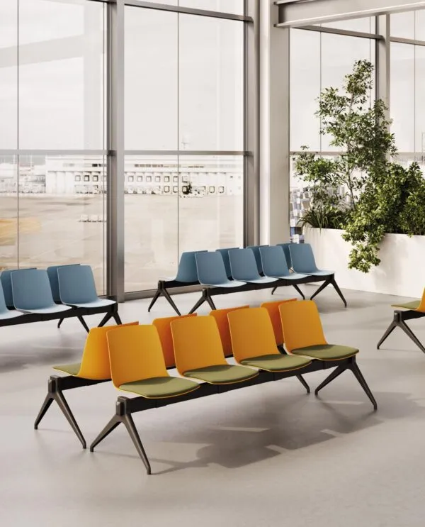 Bancs salle d'attente Yo Plastic Bench avec coques orange et coussins verts devant des bancs bleus, pieds en V inversé noirs, dans un espace d'attente lumineux Frezza