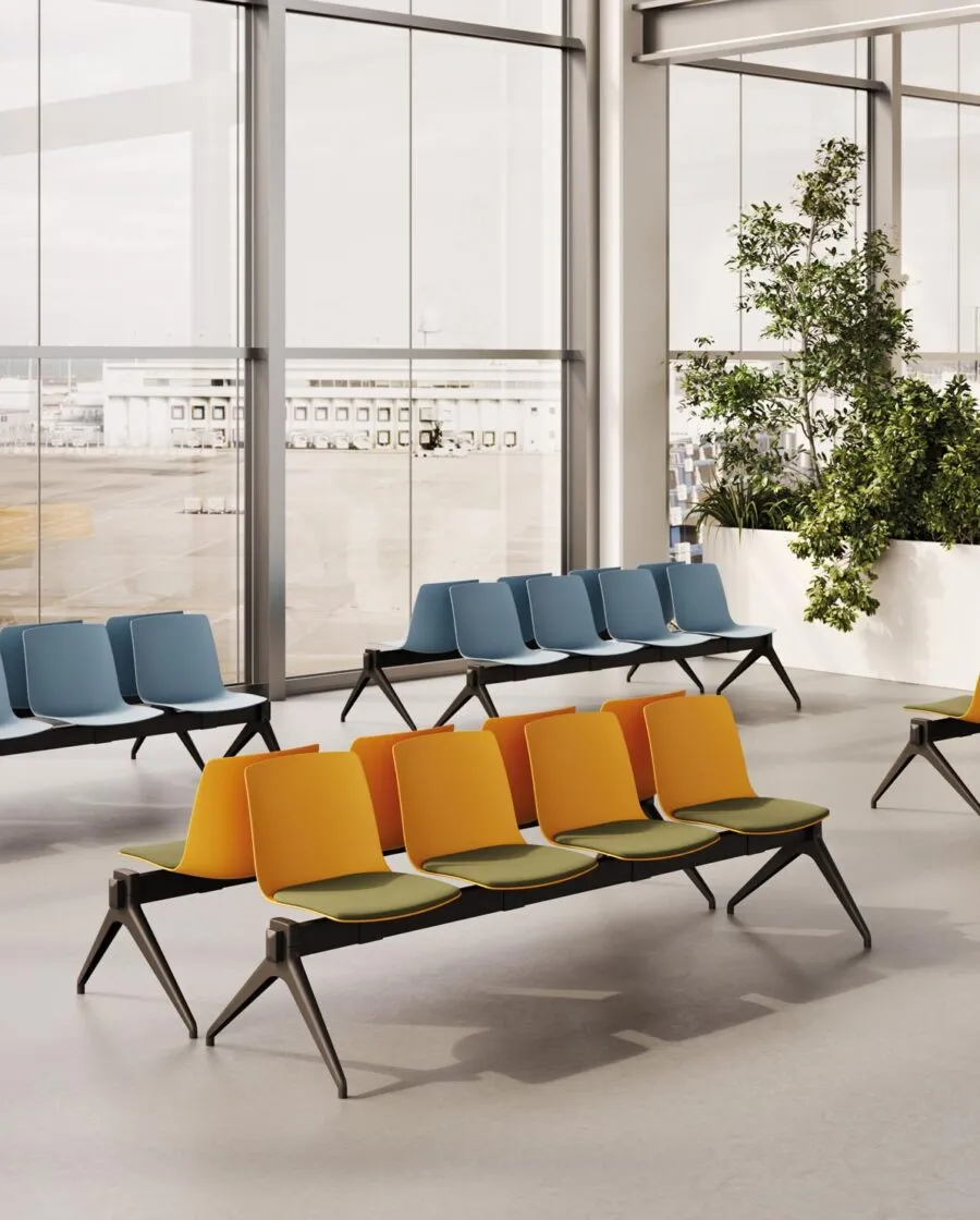 Bancs salle d'attente Yo Plastic Bench avec coques orange et coussins verts devant des bancs bleus, pieds en V inversé noirs, dans un espace d'attente lumineux Frezza