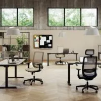 Sedie ergonomiche ufficio 8 ore Viggo in grigio e nero, con e senza poggiatesta, in un open space con scrivanie regolabili in altezza, librerie metalliche e pareti in cemento