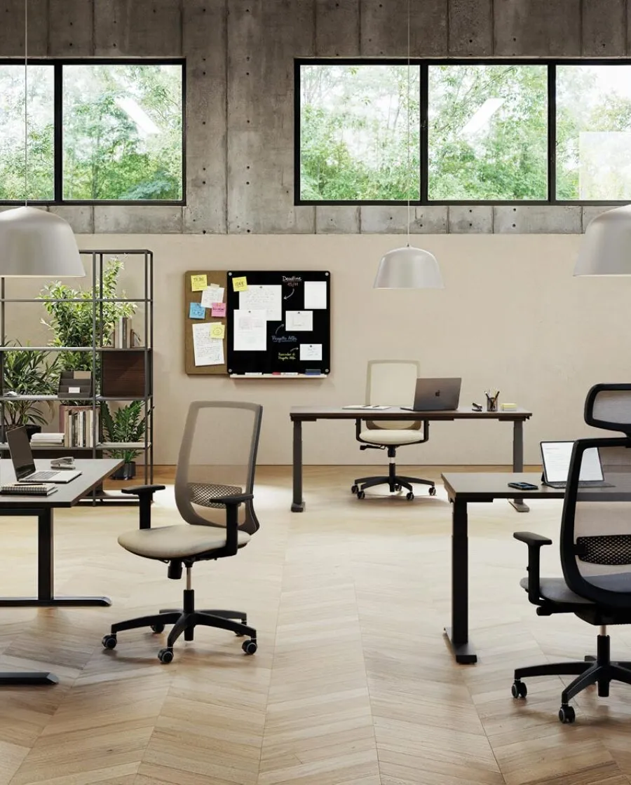 Sedie ergonomiche ufficio 8 ore Viggo in grigio e nero, con e senza poggiatesta, in un open space con scrivanie regolabili in altezza, librerie metalliche e pareti in cemento
