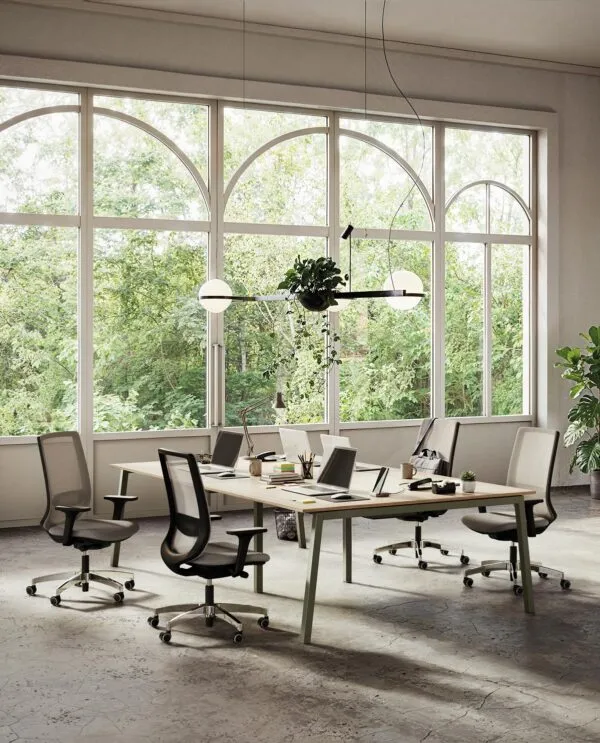 Sedie ergonomiche ufficio 8 ore Viggo in grigio con basi in nylon nero e alluminio lucido, attorno a un tavolo operativo condiviso davanti a grandi vetrate ad arco